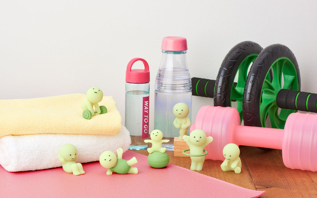 smiski exercising lifestyle image with full figures on a wooden backdrop with towels water bottles and equipment props
