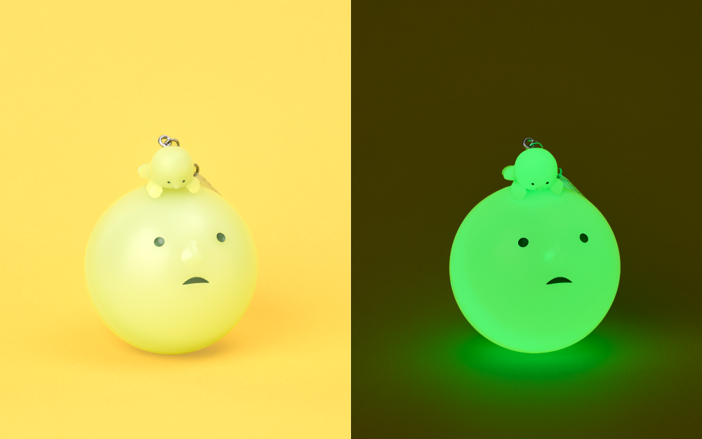 Split image shows on the left SMISKI Strap Accessories charm atop its blind ball, and on the right, the same image with SMISKI glowing in the dark