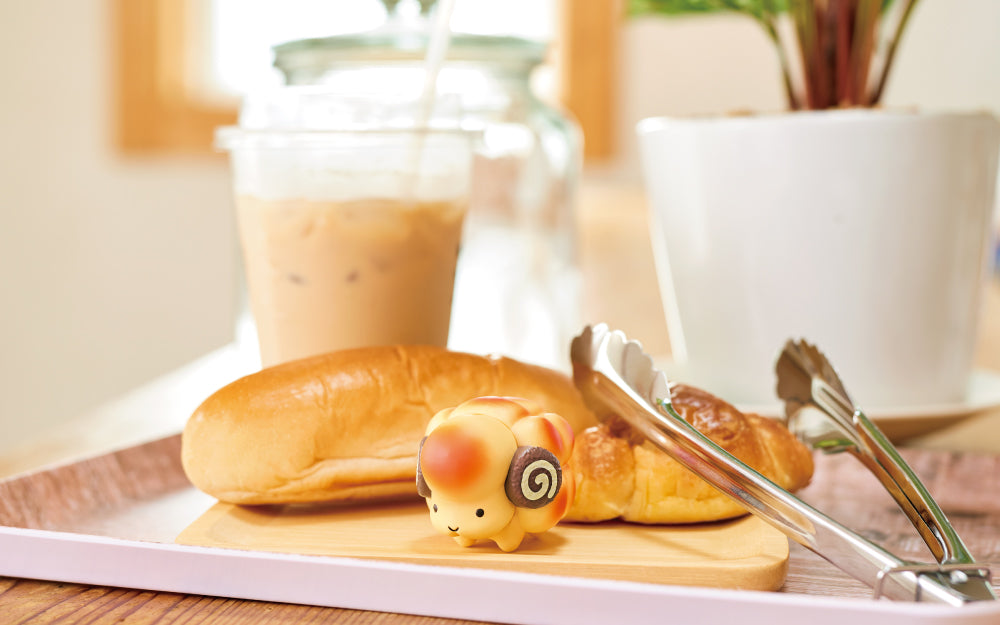 animal bakery sheep mini figure on a wooden cutting board with roll, tong, and iced coffee props