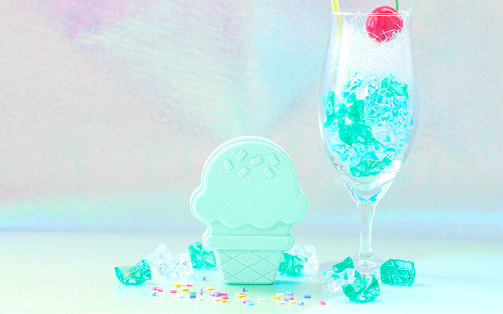 lifestyle image of ice cream cream soda rainbomb aurora on an iridescent backdrop with fake ice cube, wine glass, and sprinkles props