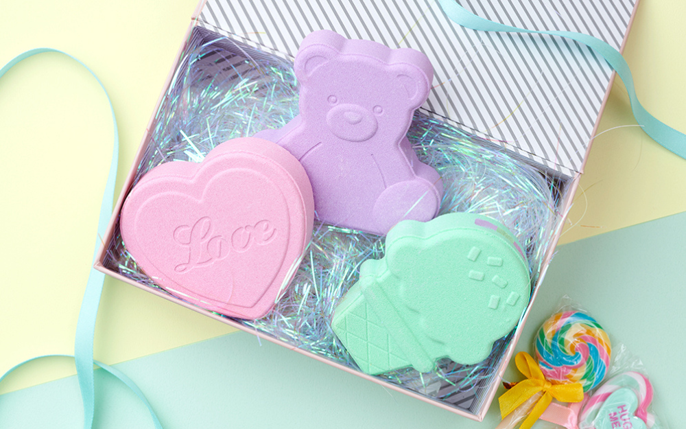 all three rainbomb aurora styles (heart floral, bear cotton candy, ice cream cream soda left to right) in a striped gift box with iridescent package fill