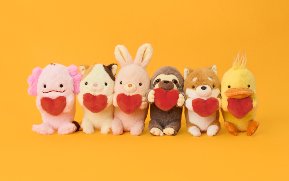 Set on a rich yellow background, image shows each of the product variants of the Funbaru Posture Pal Bag Charm; from Left to Right: Axolotl, Calico Cat, Rabbit, Sloth, Shiba Inu and Duck Bag Charms each holding a red plush heart