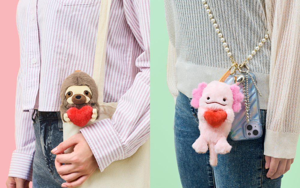Split image shows two of the Posture Pal Bag Charm variants. Left side: set against a pink background, a figure stands in a striped long sleeved shirt and jeans. Sloth Posture Pal Bag Charm sits inside the top edge of a canvas shoulder bag. Right side: set against a mint green background, a figure stands in a white sweater and jeans. Attached to a pearl beaded strap, the Axolotl Bag Charm hangs in front of a cell phone