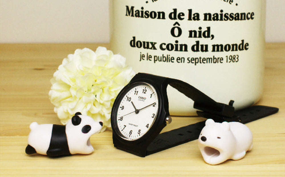 Product image shows Cable Bite- Panda, and Cable Bite- Polar Bear set on a wooden surface in front of a black wristwatch, white flower, and white ceramic container with writing on it