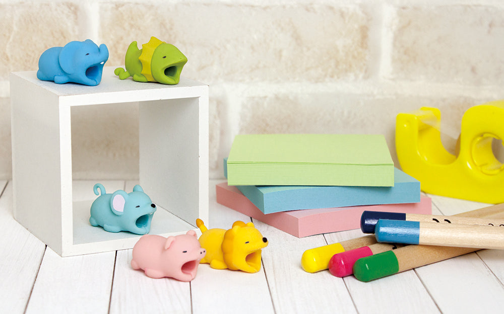 Image shows Cable Bite Volume 2 product variants beside small notebooks, a tape dispenser and several colored pencils. From top to bottom, left to right: Elephant, Frilled Lizard, Mouse, Pig, and Lion