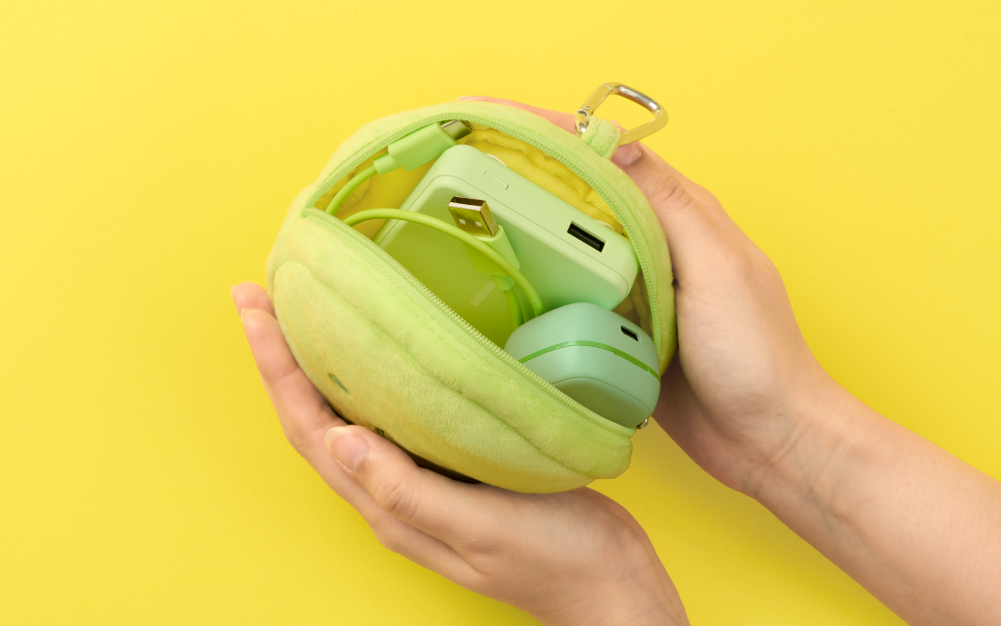 Set on bright yellow background. Unzipped SMISKI Cushion Pouch shows green charging cable, charging brick and closed earpods are seen inside. 