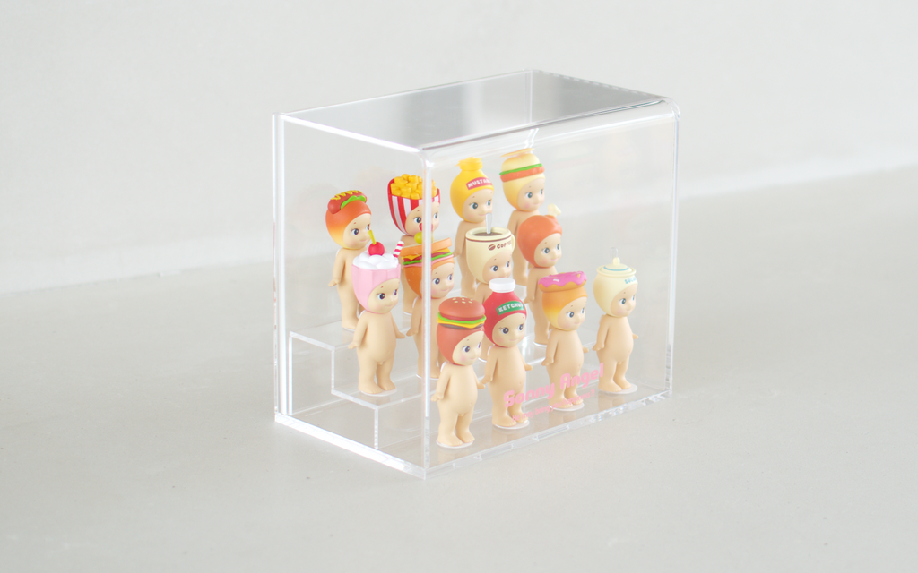 Sonny Angel clear acrylic display case shows the Snack Series in three rows. Back row: Hotdog, French fries, Mustard and Fried Chicken Sandwich. Middle row: Milkshake, Sandwich, Coffee and Fried chicken. Front row: Hamburger, Ketchup, Donut and Sugar. Pink text reads "Sonny Angel He may bring you happiness?!" on the acrylic display.
