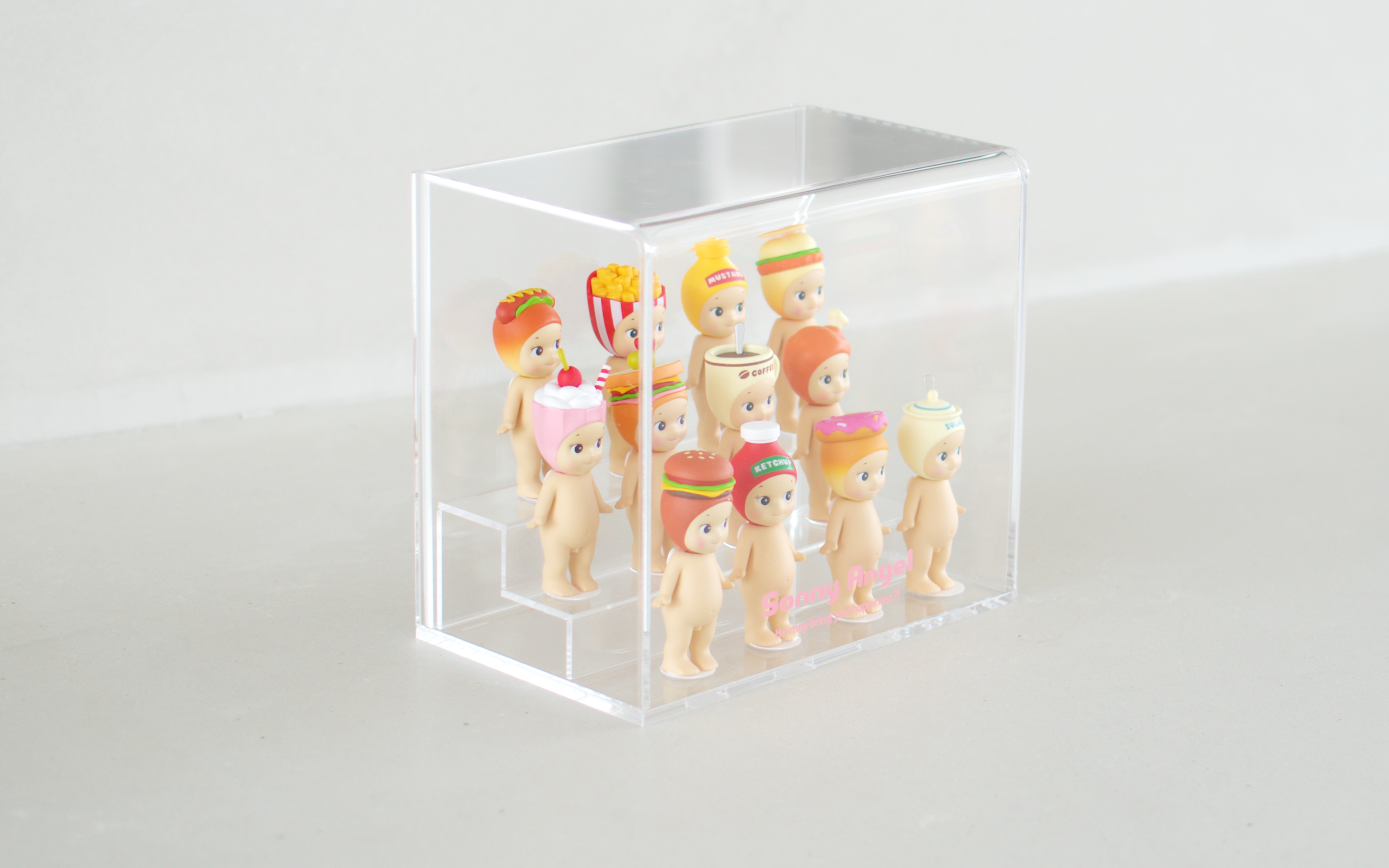 Sonny Angel clear acrylic display case shows the Snack Series in three rows. Back row: Hotdog, French fries, Mustard and Fried Chicken Sandwich. Middle row: Milkshake, Sandwich, Coffee and Fried chicken. Front row: Hamburger, Ketchup, Donut and Sugar. Pink text reads "Sonny Angel He may bring you happiness?!" on the acrylic display.