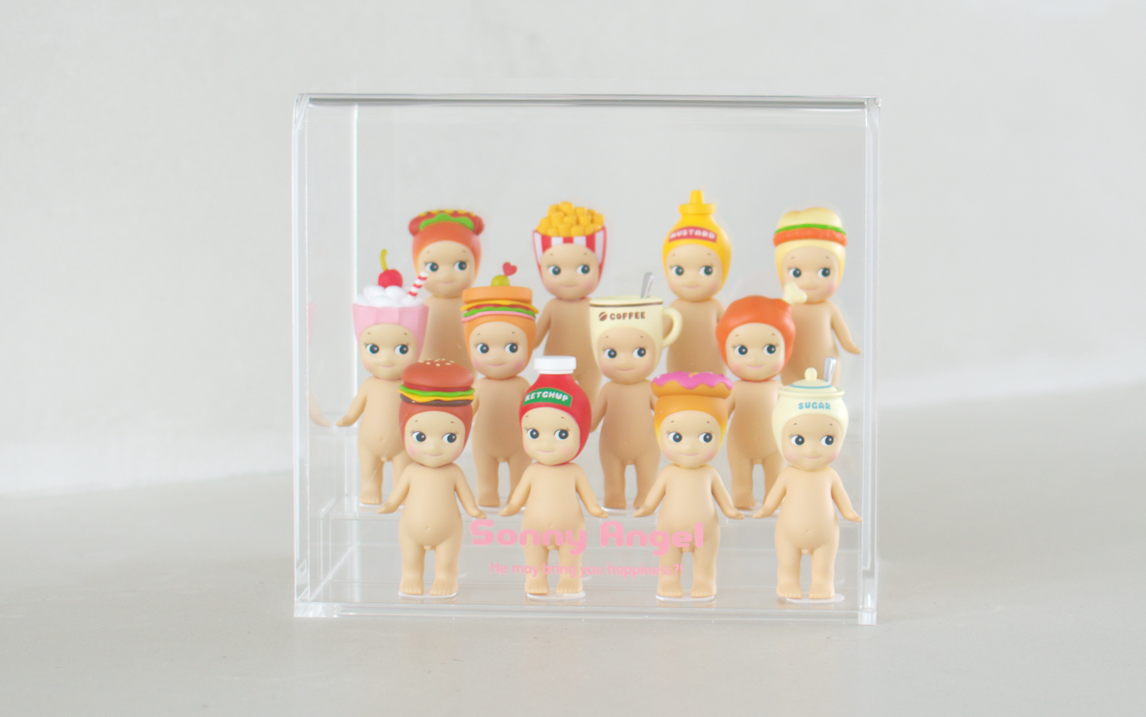 Sonny Angel clear acrylic display case shows the Snack Series in three rows. Back row: Hotdog, French fries, Mustard and Fried Chicken Sandwich. Middle row: Milkshake, Sandwich, Coffee and Fried chicken. Front row: Hamburger, Ketchup, Donut and Sugar. Pink text reads "Sonny Angel He may bring you happiness?!" on the acrylic display