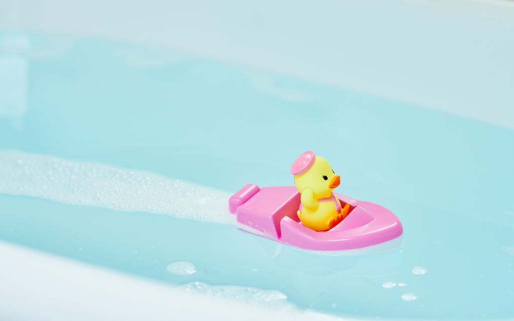 closeup of pink duck sailor boat in blue bath tub water; boat is being propelled forward by bath tablet