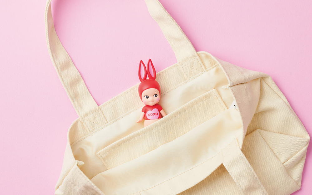 Product showcase of the Kiss Kiss Rabbit minifigure peeking out halfway from the pocket in the Kiss Kiss Tote