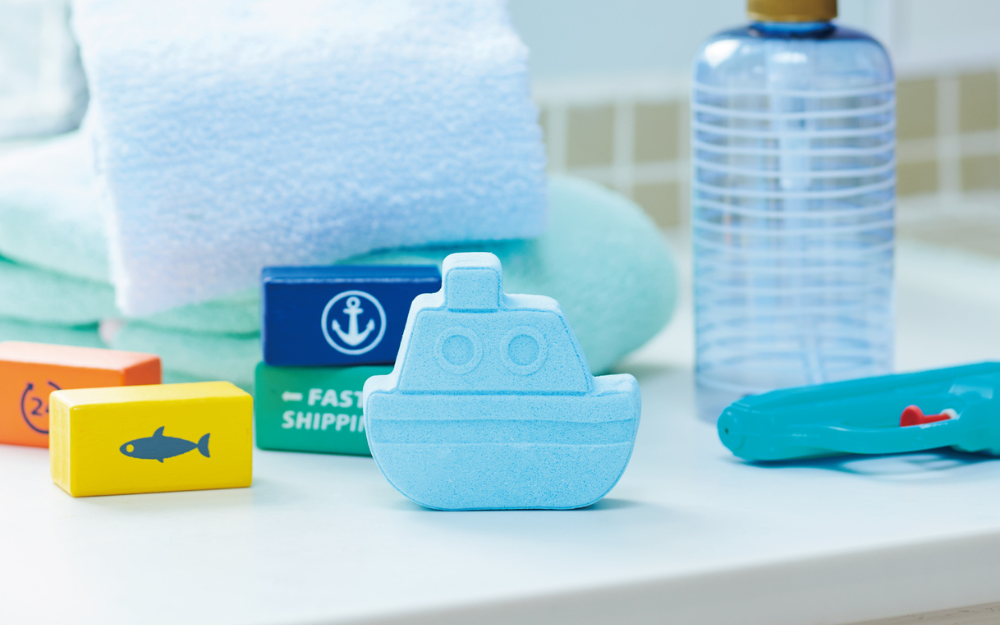 rainbomb mini blue boat on a white bathroom set with wooden block water gun, soap bottle, and towel props