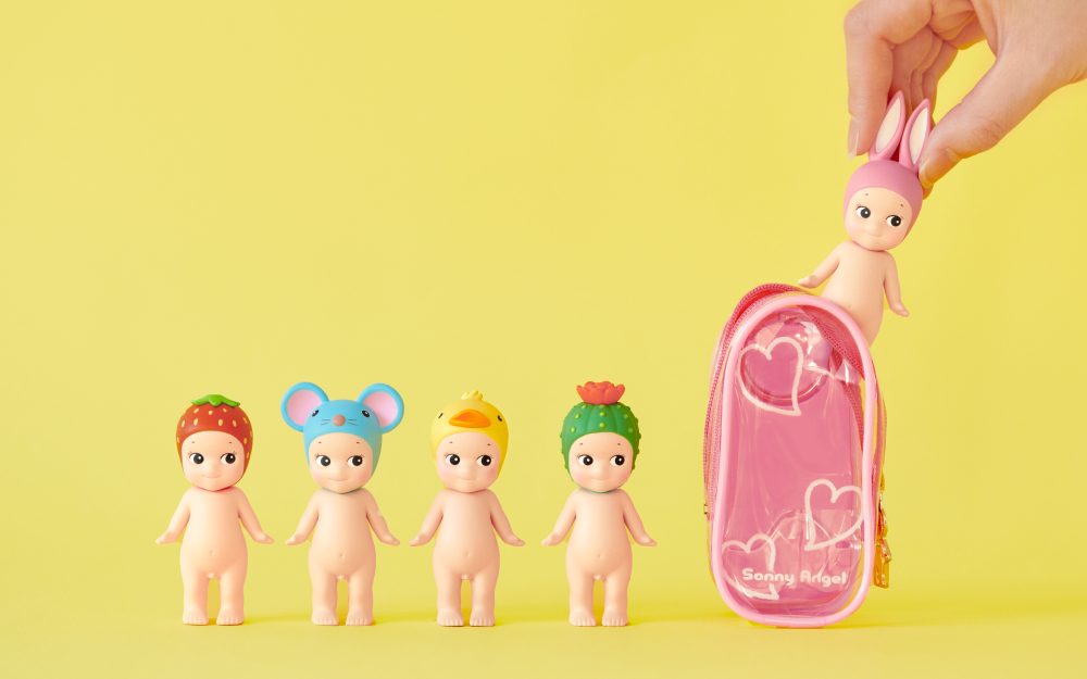product lifestyle image of my bestie case pink with five minifigures against a yellow backdrop. lineup from left to right, strawberry, mouse, duck, cactus, and rabbit. hand is placing or removing sonny angel rabbit figure inside my bestie case pink.