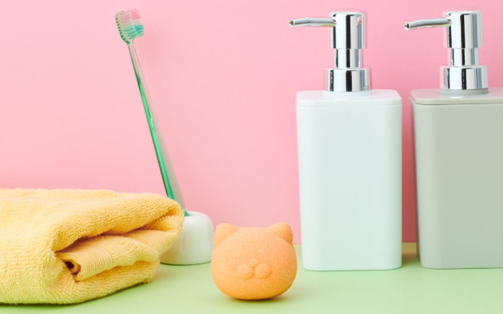 Product image for Nekomote Bath Bomb- Chamomile scent. Set against a light pink background, atop a mint green countertop image shows a folded yellow towel, green toothbrush, white and silver pump dispensers sits a Nekomote Bath Bomb- Chamomile scent