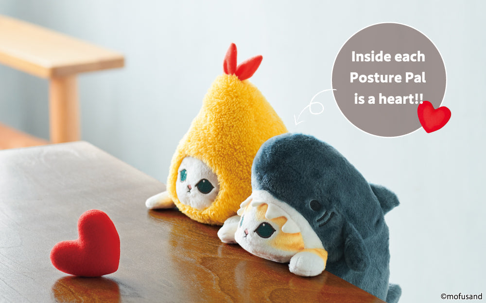 mofusand Posture Pal image shows Shrimp Meow and Shark Meow Posture Pal products sat at a wooden table against a pale blue background. In front of the Posture Pals, on the table sits a red plush heart. Text above product states "Inside each Posture Pal is a heart!!" with a red heart icon. 