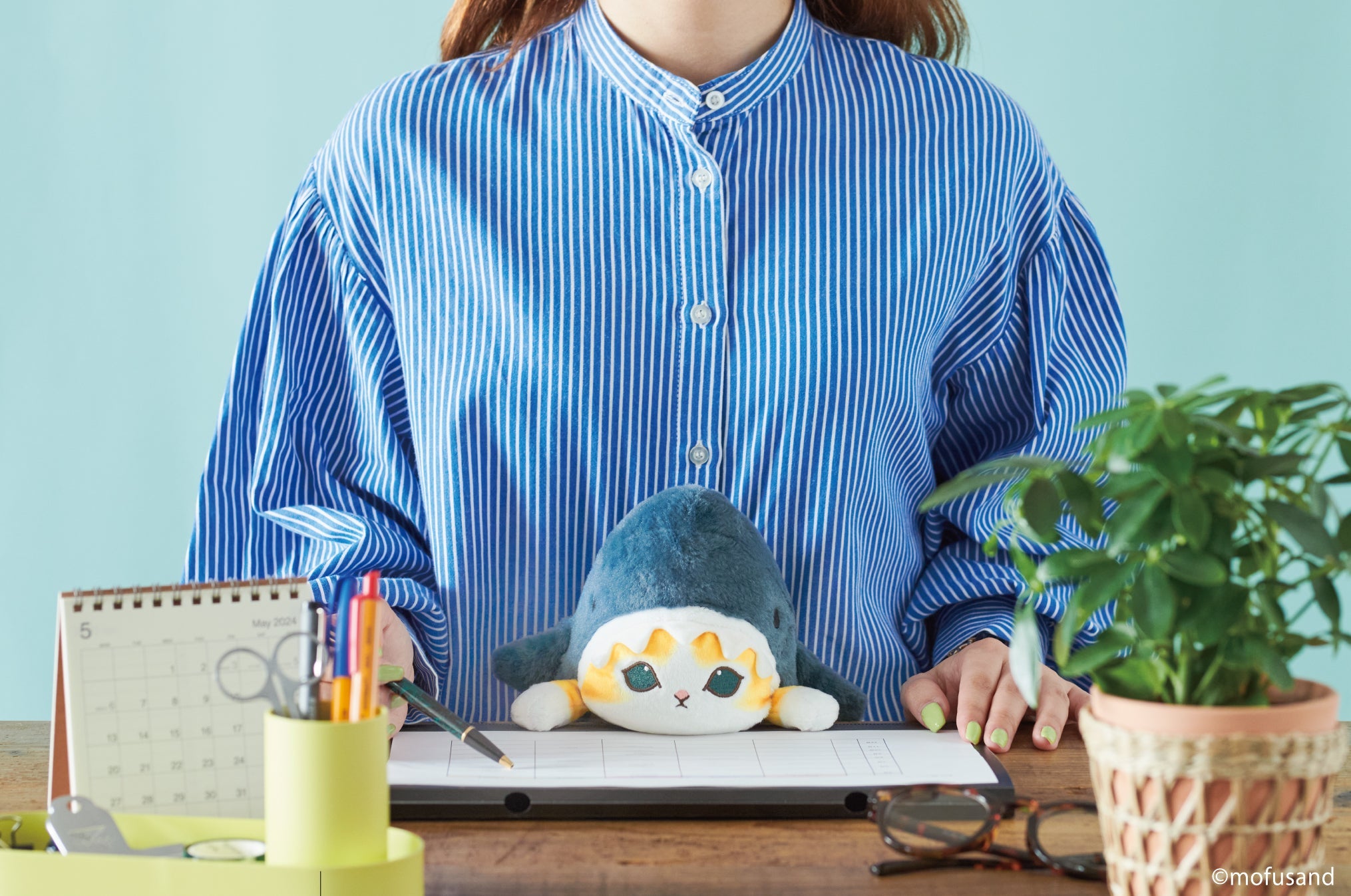 lifestyle image of mofusand posture pal shark meow. features front facing view of person wearing blue striped shirt writing on a planner and using posture pal shark meow.