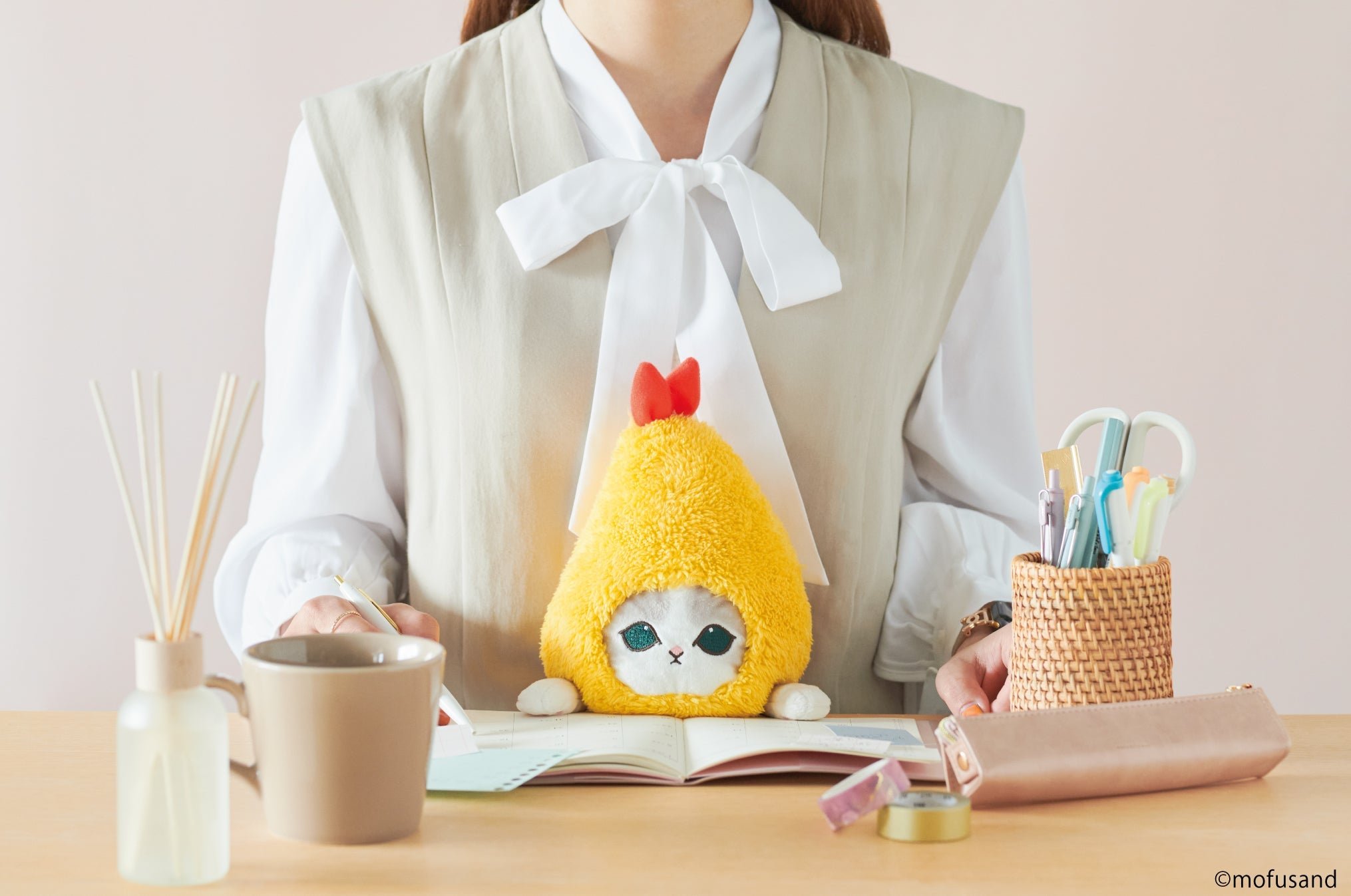 lifestyle image of posture pal mofusand shrimp meow. features a front facing view of person in a gray blouse writing in a planner using shrimp meow at desk