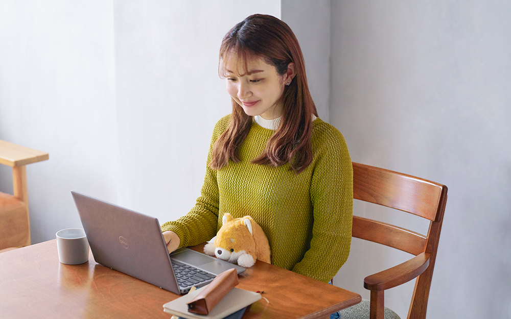 product lifestyle image feturing a person sitting at a table with a laptop. they have the shiba inu posture pal from posture pal volume 2 between their abdomen and the edge of the table and are smiling