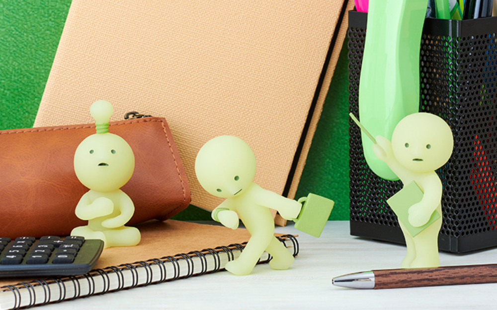 closeup of smiski idea, briefcase, and presentation on a desk backdrop with office supply props