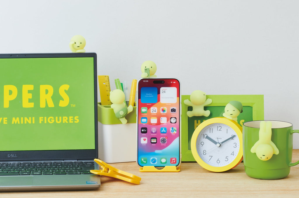 product lifestyle image for the smiski hippers minifigure series featuring the main lineup. from left to right: looking out attached to laptop; climbing attached to pencil holder; on his phone attached to a phone case; sticking attached to a picture frame; dozing attached to an analog clock; upside down attached to a mug.