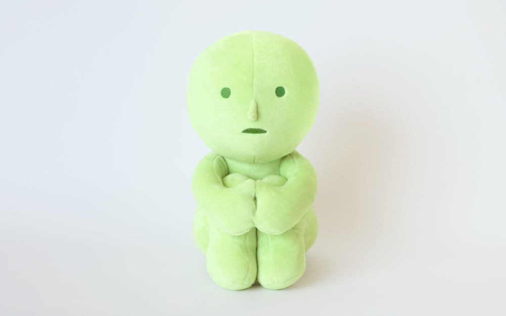 Set on light grey background. "Hugging Knees" SMISKI plush sits hugging knees to chest. 