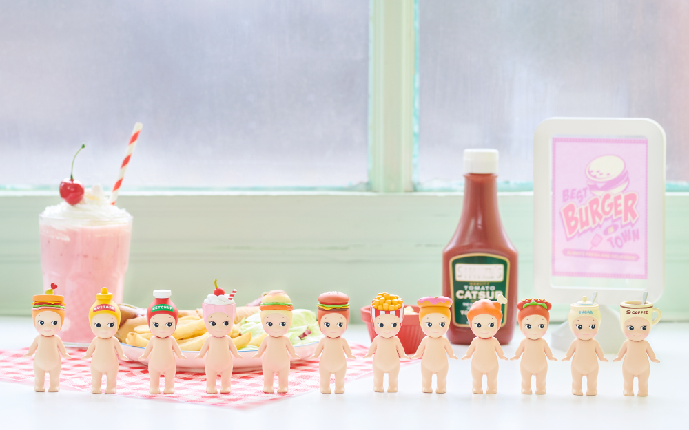 sonny angel snack series minifigure banner featuring minifigures in a row; sandwich, mustard, ketchup, milkshake, chicken sandwich, cheeseburger, french fries, donut, chicken leg, hotdog, sugar and coffee minifigures stand on a table in front of a milkshake, plate of hotdog and fries, ketchup bottle, and BEST BURGER IN TOWN sign.