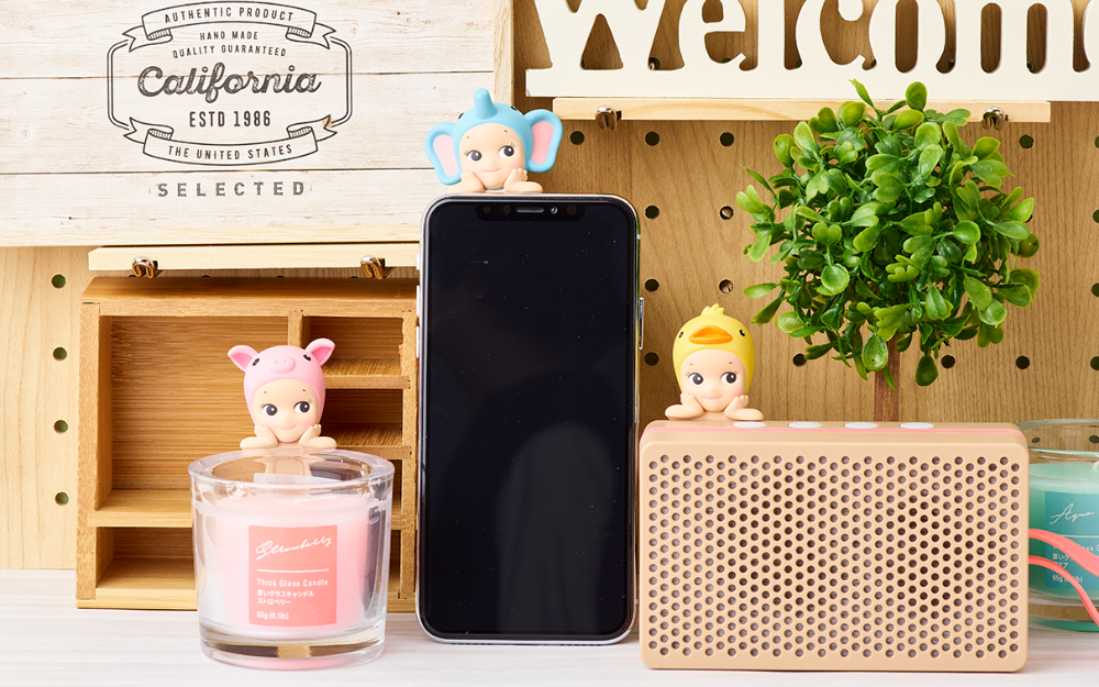 sonny angel hippers minifigure lifestyle image with pig attached to candle, elephant attached to phone, and duck attached to speaker props. other props include fake plants and wooden box