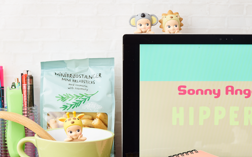 sonny angel hippers mini figure lifestyle image with giraffe attached to coffee mug and koala and lion attached to a laptop with the words SONNY ANGEL HIPPERS. other props include pen cup and mini breadsticks snack bag