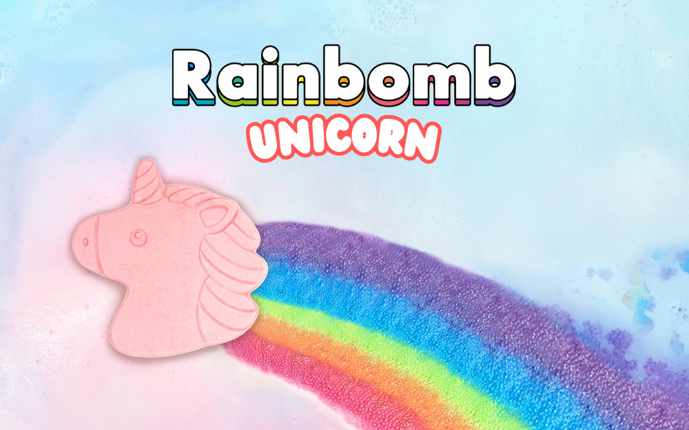 A unicorn-shaped bath bomb with a colorful rainbow mane and tail, displayed against a blue background with the product name 'Rainbomb Unicorn' at the top.