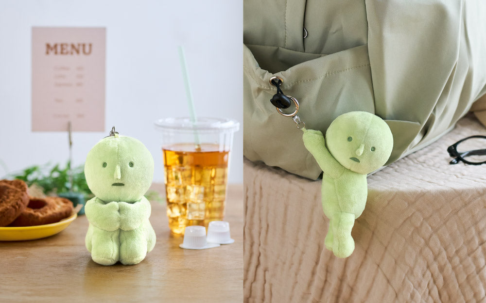 Two photos. Left: White background with a light brown "MENU" on the wall out of focus. (Left) Below the MENU is a yellow plate with two old fashioned donuts on a wood table. The SMISKI Hugging Knees Plush Keychain (Middle) sits between the donuts and an iced tea. Right: SMISKI Hanging On Plush Keychain clipped to a beige drawstring bag set on a table covered in a light tan muslin tablecloth. There is a  pair of glasses with round black frames to the right of the bag on the table, mostly cut off.