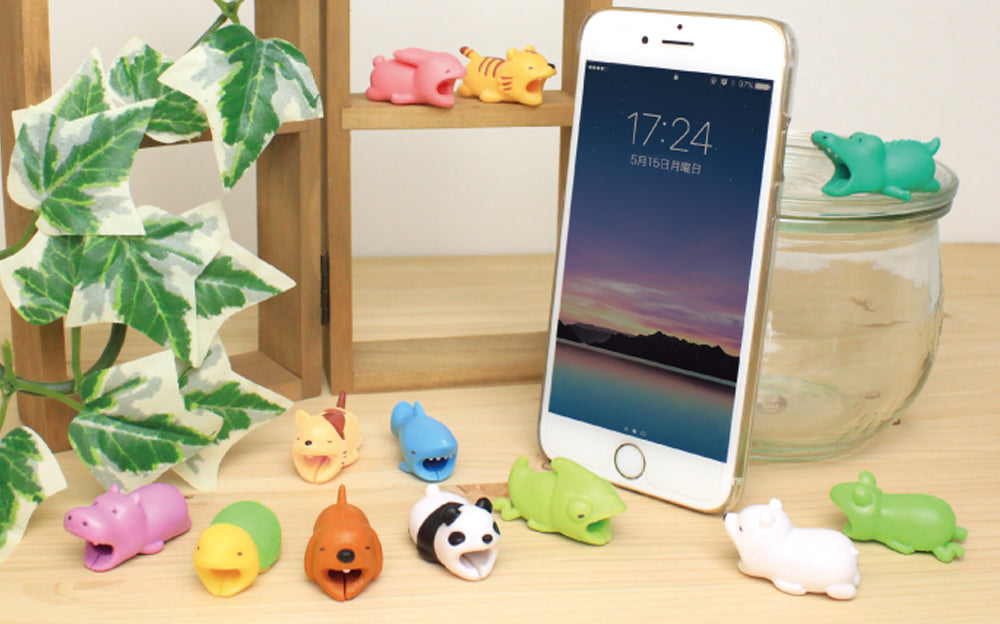 Image shows all product variants for Cable Bite Vol. 1 Cable Accessory. On top of a wooden frame shelf, Rabbit and Tiger. On a wooden tabletop beside green ivy, Hippopotamus, Turtle, Dog, Panda and Chameleon; in the row behind: Cat and Shark. To the right of an white iPhone, Polar Bear, Frog and above on a glass dish, Crocodile